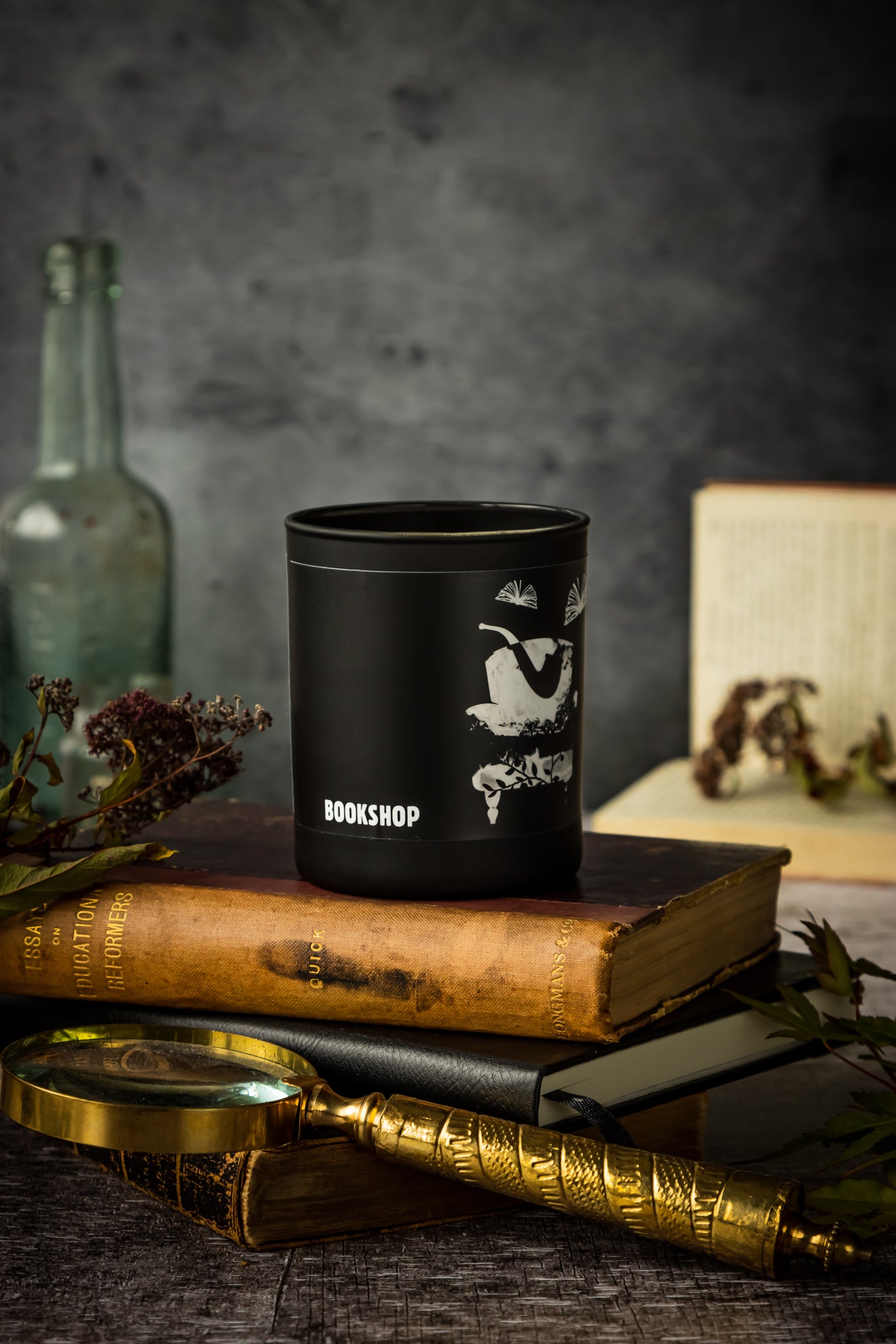 Bookshop scented candle in matte black glass jar stacked on top of old leather-bound books