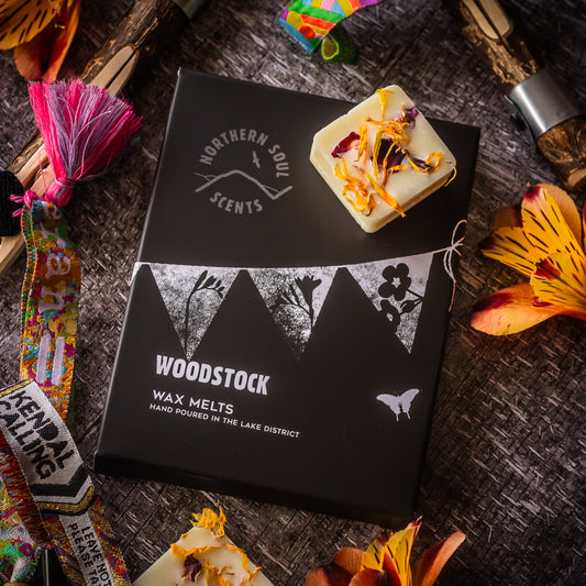 Woodstock Scented Wax Melts: Channel the spirit of music and celebration with these vibrant scented wax melts. Packaged in a plastic-free wax paper bag and enclosed in a cardboard sleeve adorned with a festive bunting design on the front, these melts capture the essence of the iconic Woodstock festival. Each wax cube is adorned with real dried flower petals, adding a touch of natural beauty