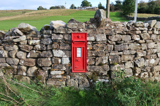 Red Royal Mail postbox set into a stone wall in scenic location 