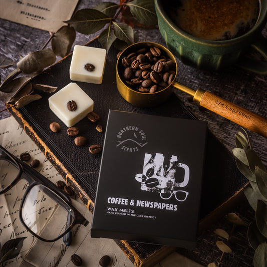 Coffee and Newspapers Scented Wax Melts. Packaged in a plastic-free wax paper bag and enclosed in a cardboard sleeve adorned with a quirky mug and coffee bean design on the front, these melts create an inviting atmosphere. Each wax cube is uniquely decorated with real coffee beans, adding a touch of charm. Experience the rich fragrance of freshly brewed coffee and the comforting scent of newspapers, perfect for creating a cozy and relaxing ambiance in any space